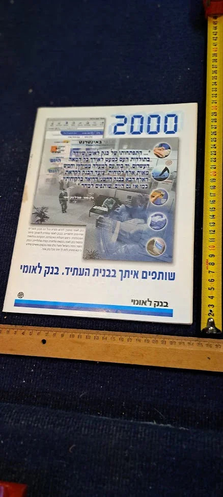 Vintage Hebrew flyer with blue text and images, placed next to measuring tape and ruler on dark fabric