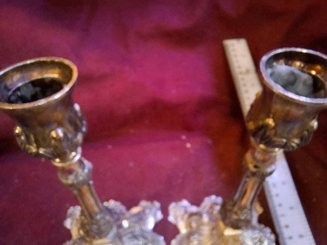 Pair of ornate vintage brass candle holders with decorative bases on a burgundy surface