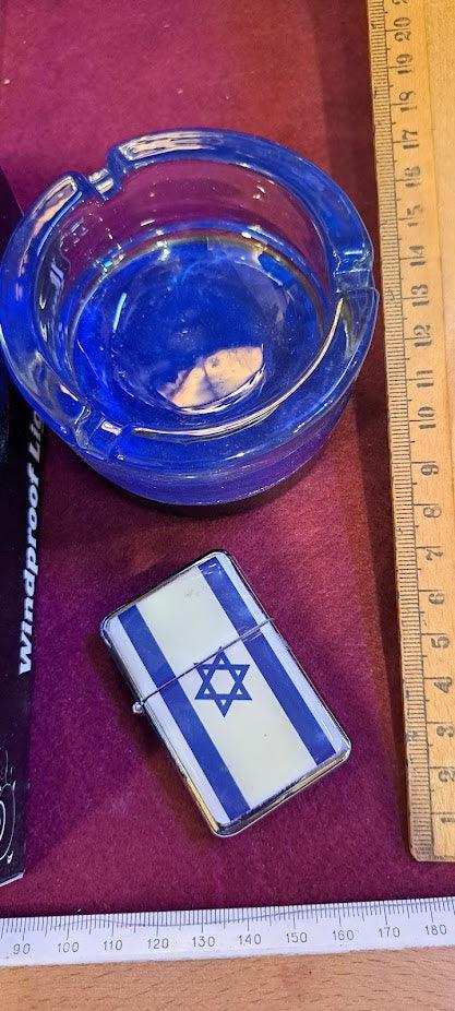Vintage blue glass ashtray and metal lighter with Israeli flag, displayed with rulers on a red surface.