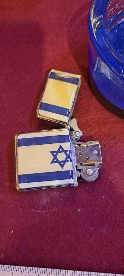 Vintage metal lighter with Israeli flag design on red surface near blue glass dish