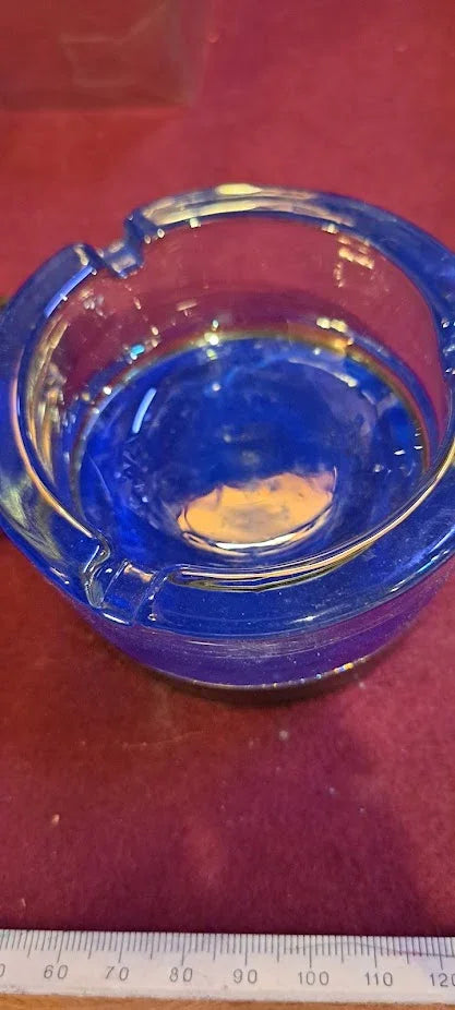 Vintage cobalt blue glass ashtray on a red surface with ruler for scale