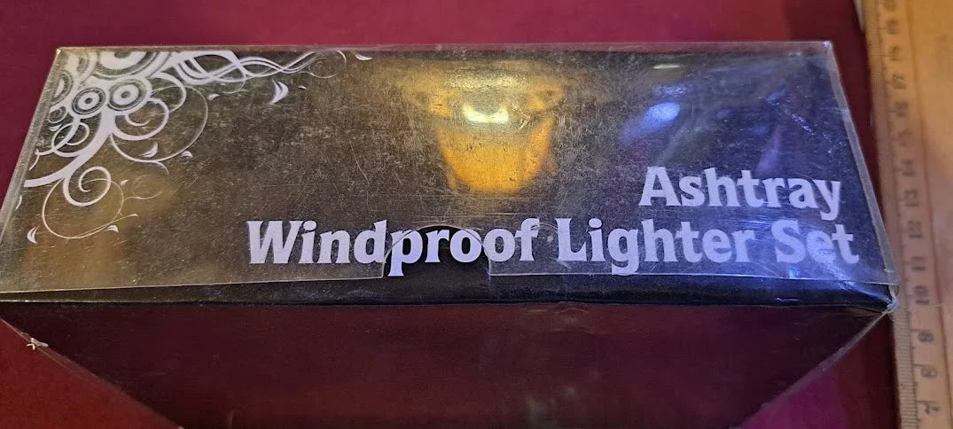 Box labeled ashtray windproof lighter set on a red surface with decorative design