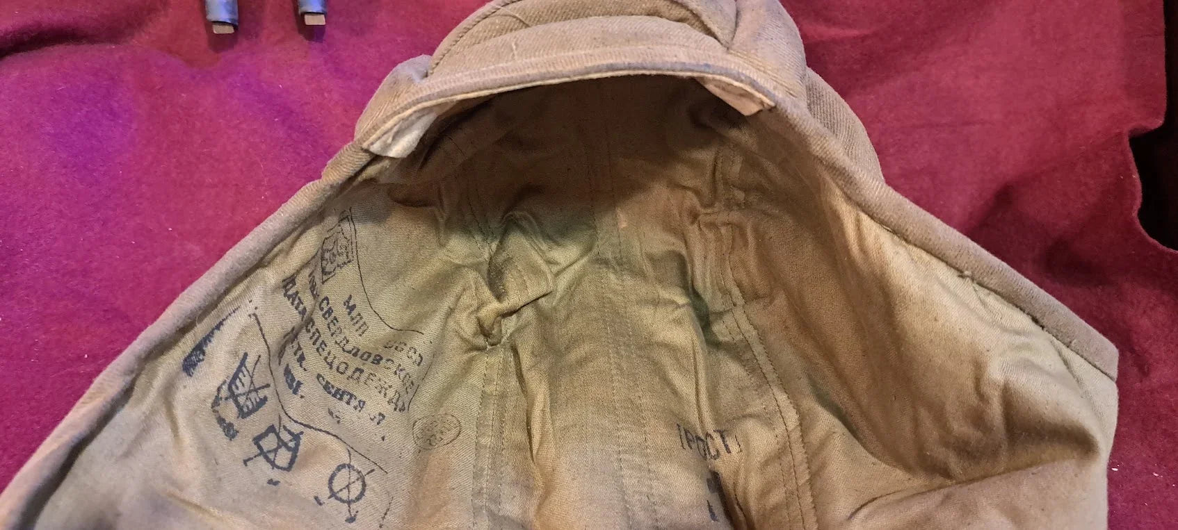 Vintage khaki military cap interior with Cyrillic markings on a burgundy background