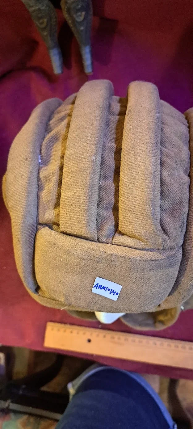 Vintage padded cloth helmet with label, displayed on a red surface with ruler for scale