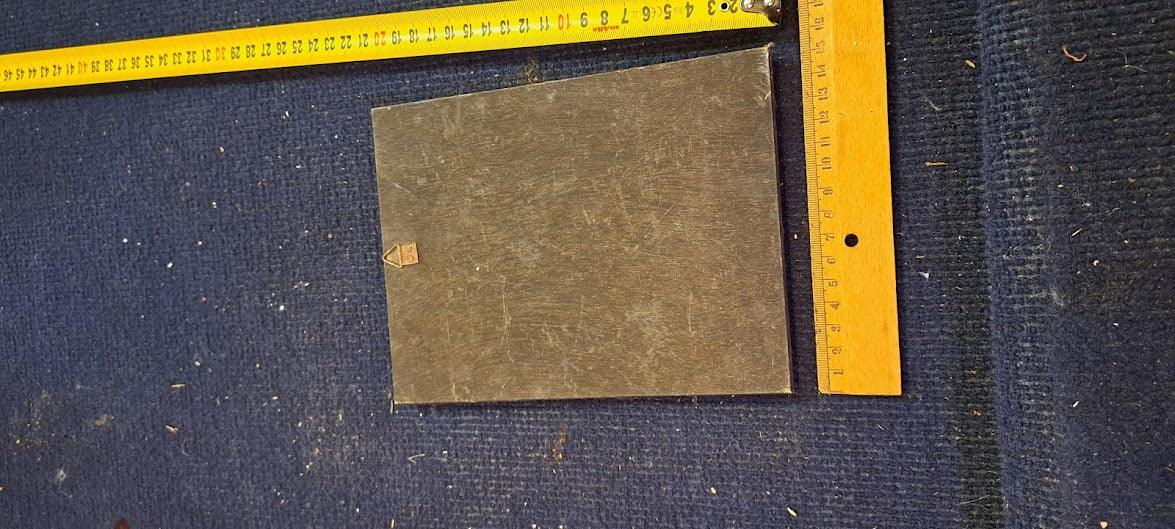 Vintage rectangular metal plate on blue carpet with tape measure and ruler for scale