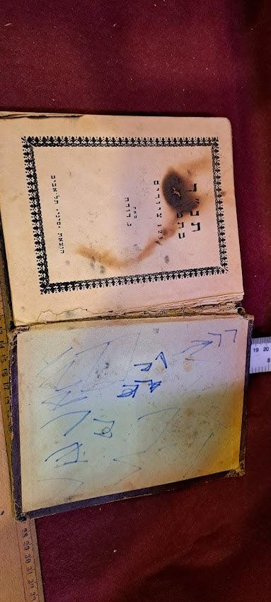 Vintage Hebrew book with burn marks and handwritten notes on a red surface