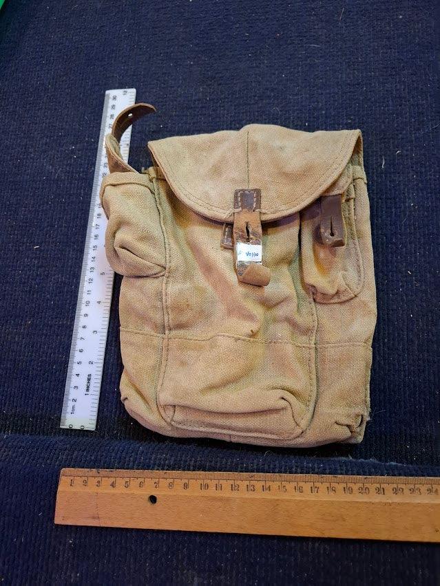 Vintage canvas military pouch with leather straps, displayed next to rulers for scale