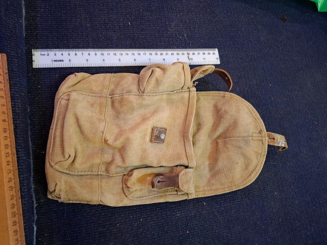 Vintage canvas pouch with leather strap, displayed on dark fabric with measuring rulers