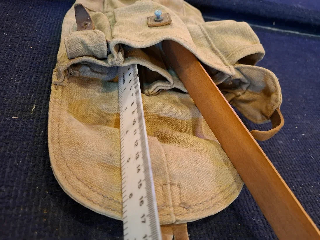 Vintage canvas tool roll with measuring stick and wooden handle on dark fabric surface