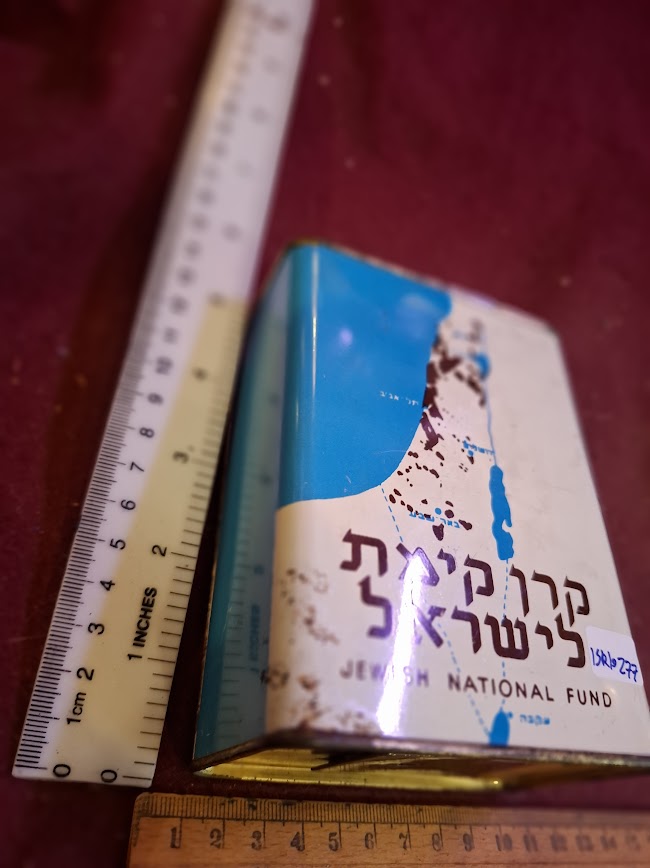 Vintage Jewish National Fund blue tin charity box with rulers for scale on maroon surface