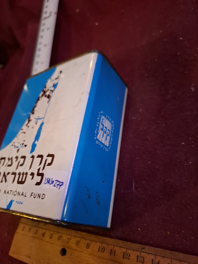 Vintage blue and white Jewish National Fund metal charity box with Hebrew text on maroon surface