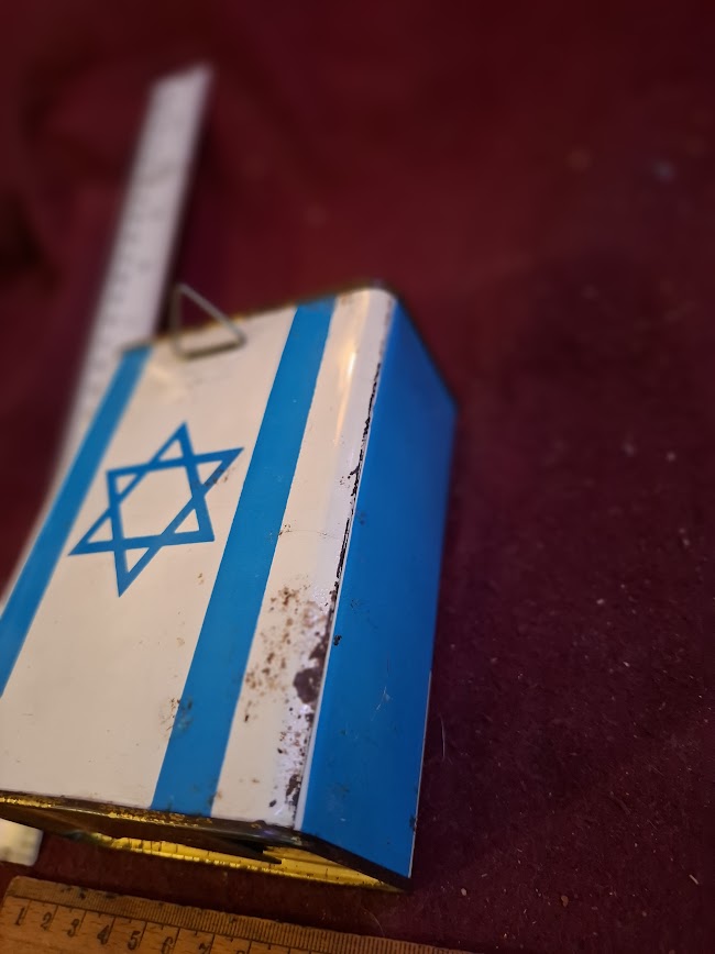 Vintage blue and white tin donation box with Star of David and ruler on burgundy surface