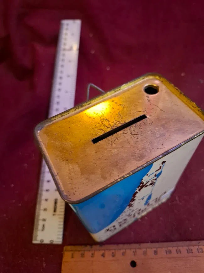 Vintage metal coin bank with slot opening, measuring rulers, maroon fabric background