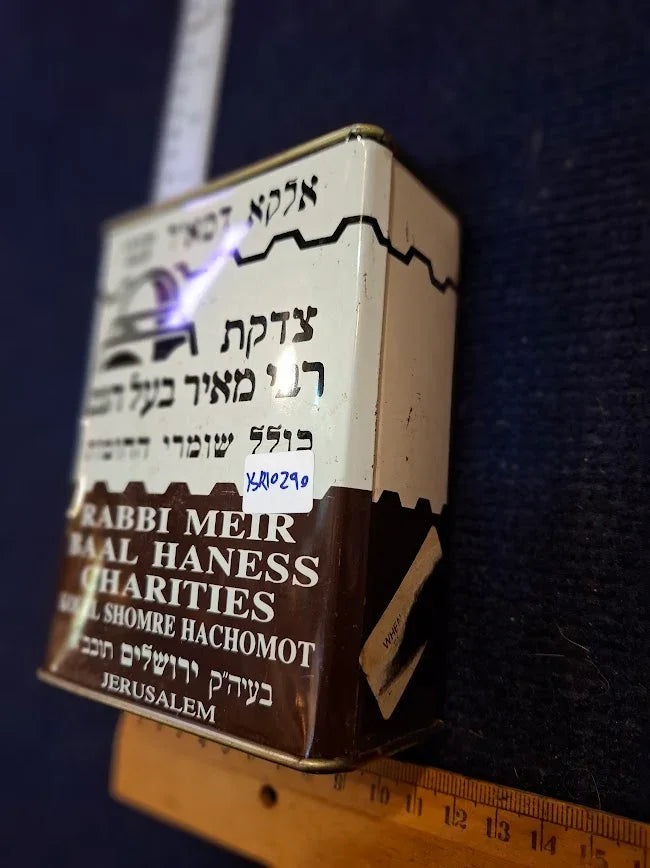 Vintage Rabbi Meir Baal Haness metal charity box with Hebrew and English text, ruler nearby