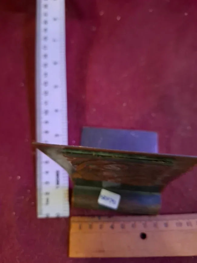 Antique metal bookend with visible rulers on a red surface, vintage collectible item