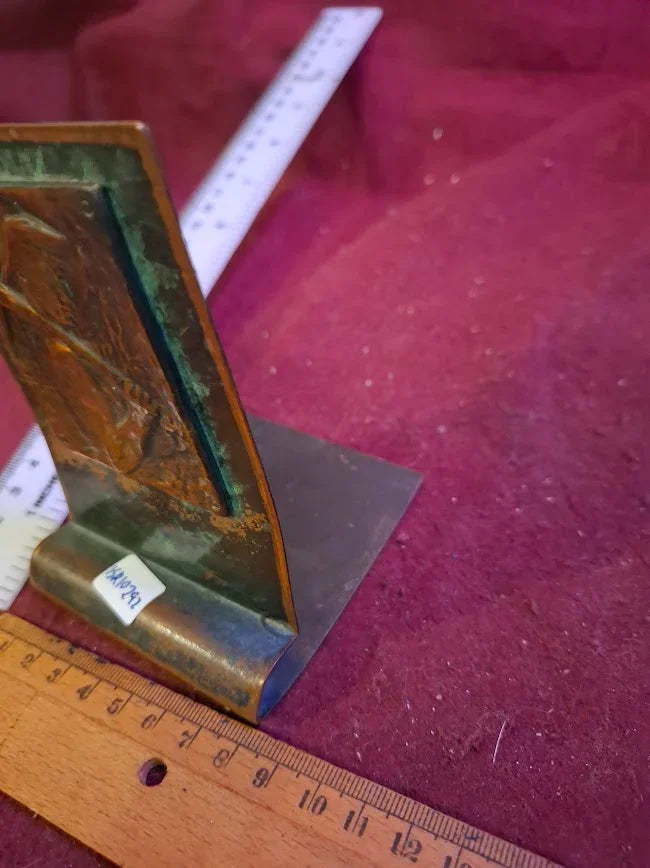 Vintage metal bookend with patina, displayed on a red velvet surface with rulers.