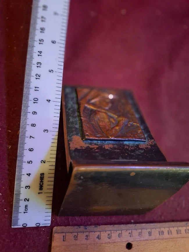 Antique decorative metal box with embossed lid, shown with rulers for size reference