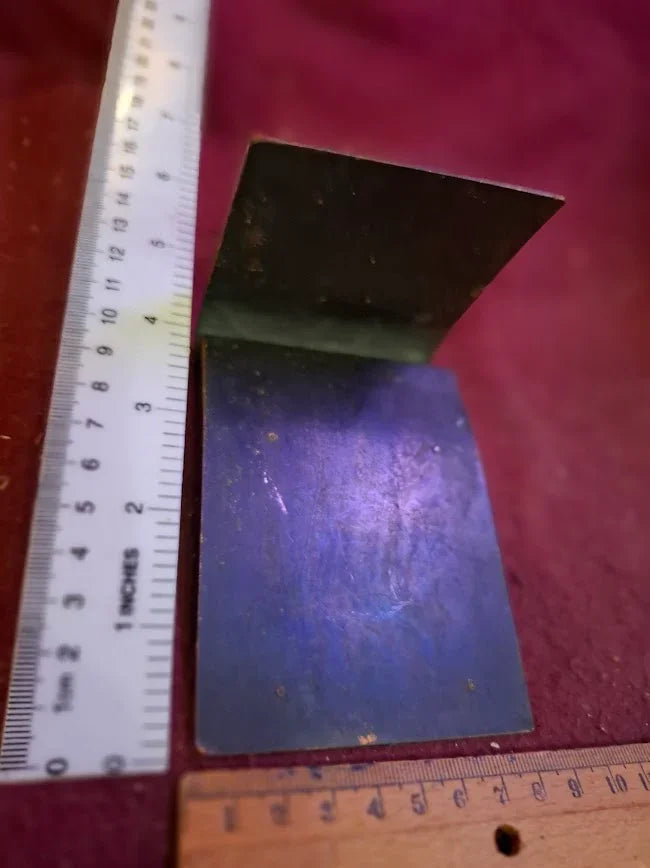 Vintage metal bracket or bookend with patina, shown with rulers for scale on red surface