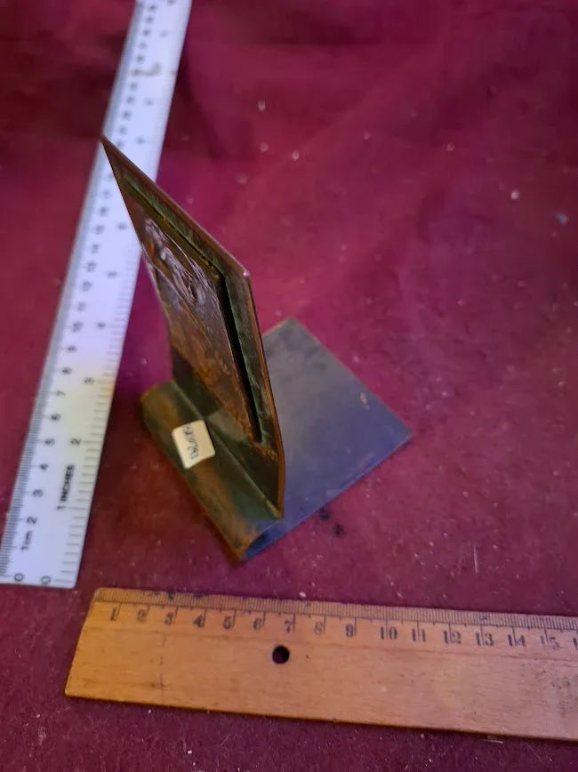 Vintage metal plaque on stand with rulers for scale on a red surface