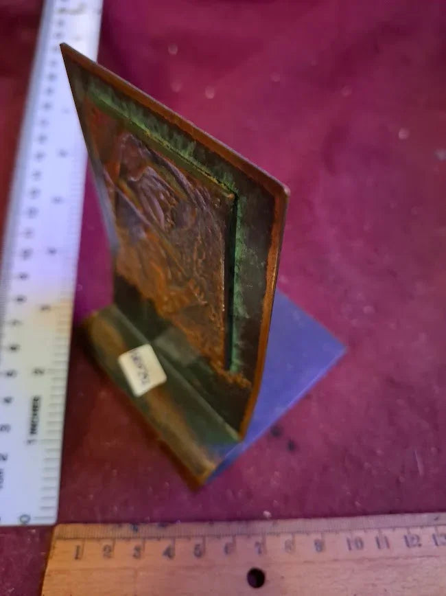 Vintage embossed metal plaque with patina on a stand, measured by rulers, on purple fabric