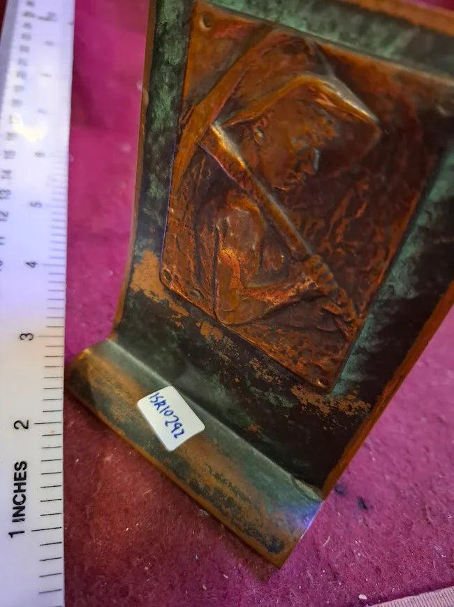 Antique copper bookend with embossed miner design, ruler for scale, collectible decor