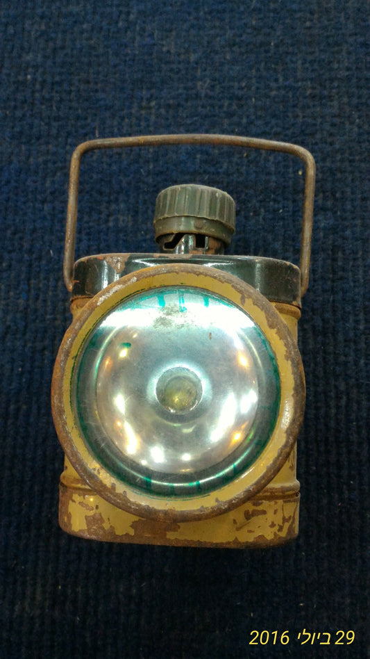 Vintage metal flashlight with handle and round lens, showing rust and wear on blue fabric