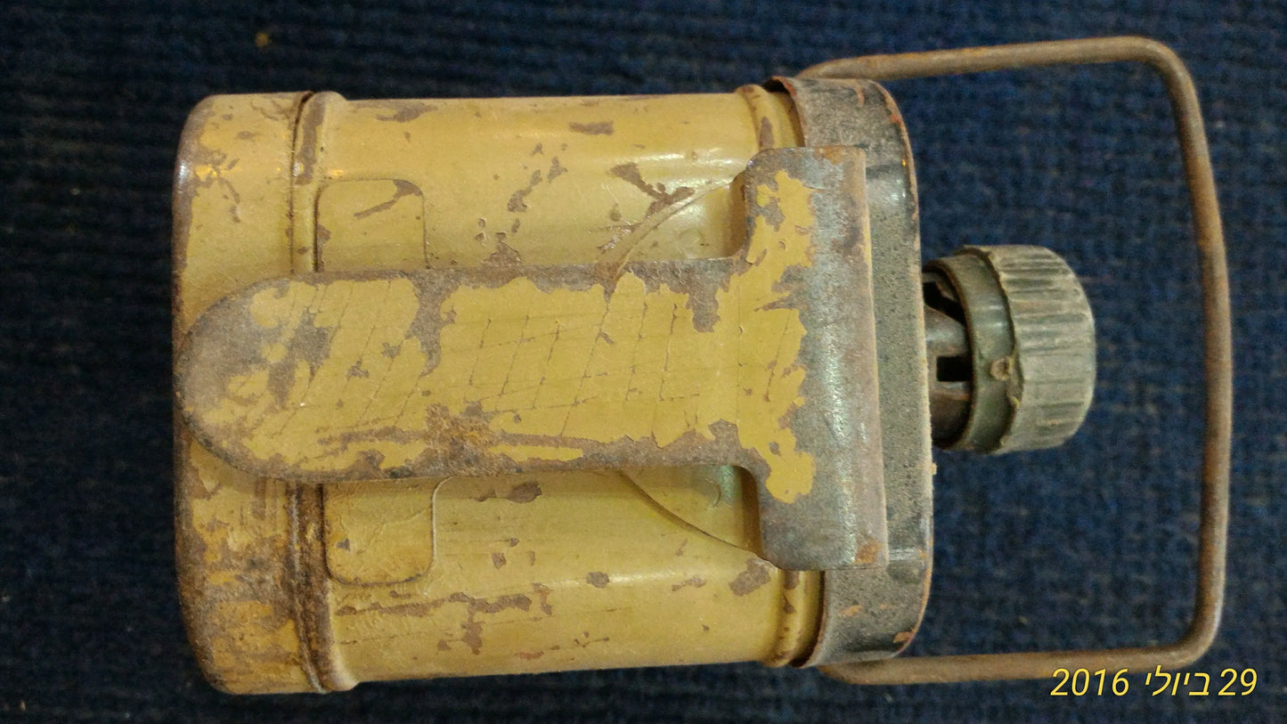 Vintage yellow metal flashlight with handle and visible rust, shown on dark textured surface