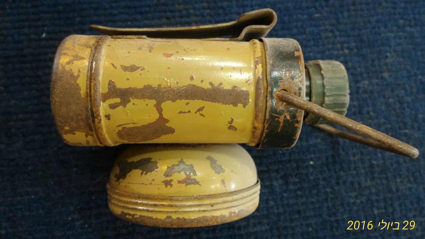 Vintage yellow metal flashlight with rust and wear, shown on dark blue fabric background.
