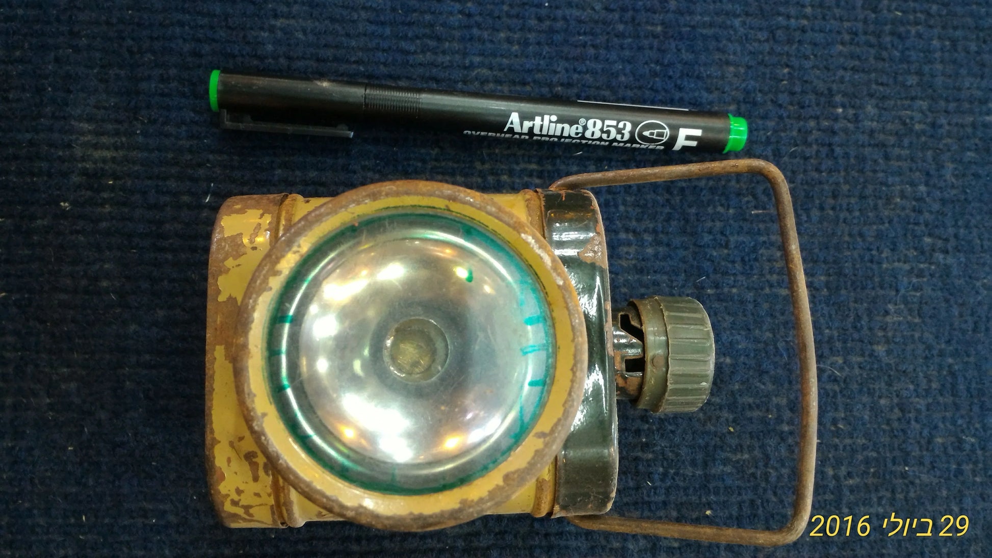 Vintage yellow metal flashlight with glass lens and handle on blue background, Artline 853 marker for scale