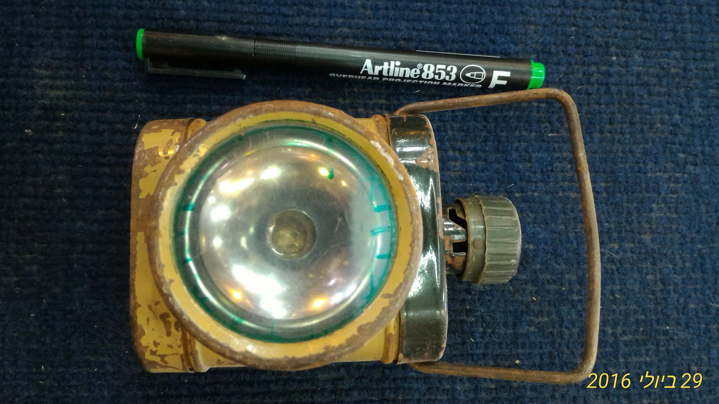 Vintage yellow metal flashlight with a large round lens and rusted handle on blue fabric background