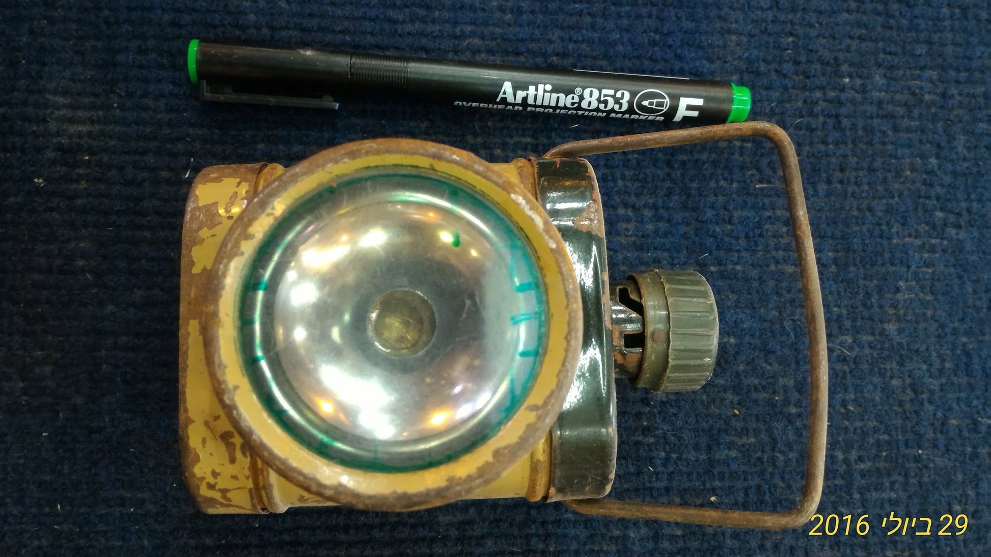 Vintage yellow metal flashlight with a large round lens and rusted handle on blue fabric background
