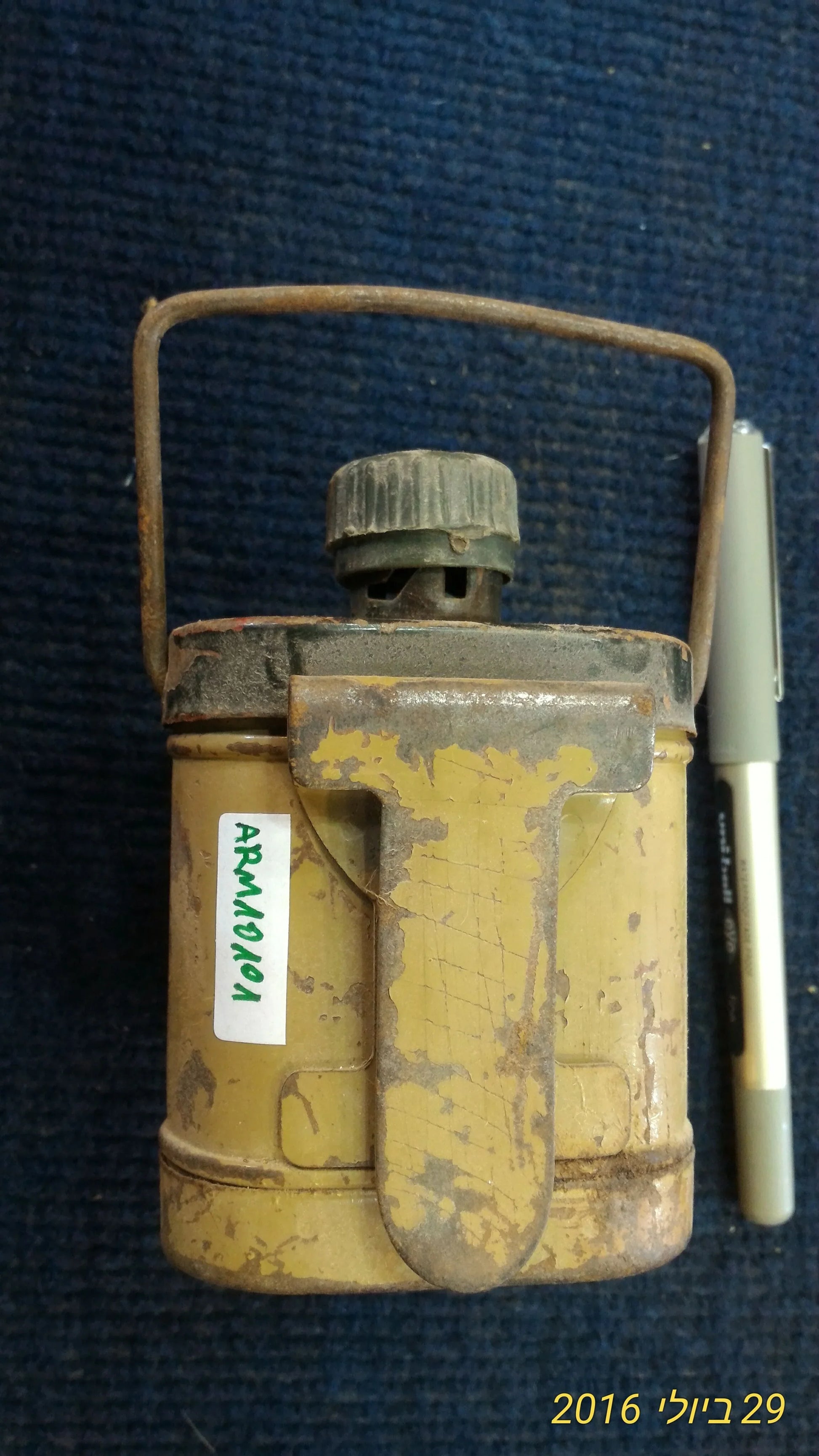 Vintage metal canister with handle and clip, distressed yellow paint, on blue surface